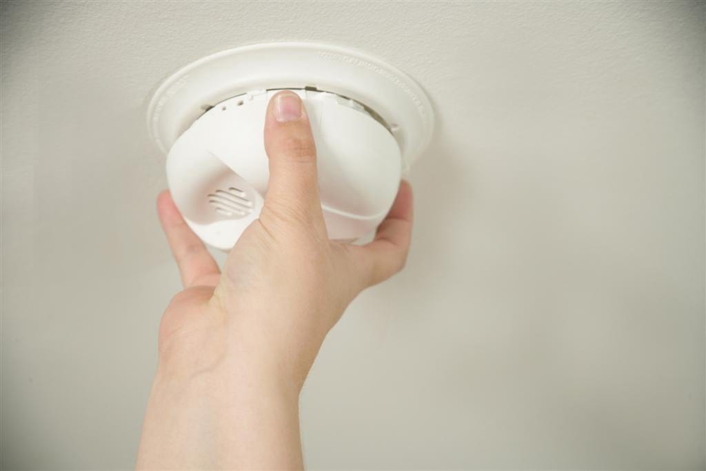Close-up of a hand checking a ceiling smoke alarm