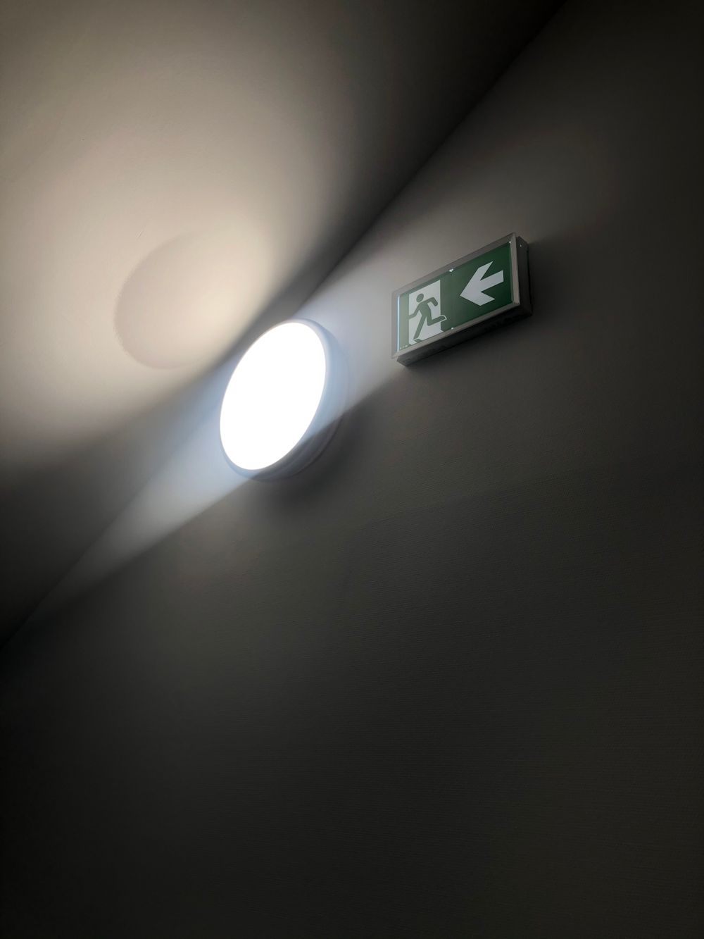 Wall light beside a green running-man escape-route sign